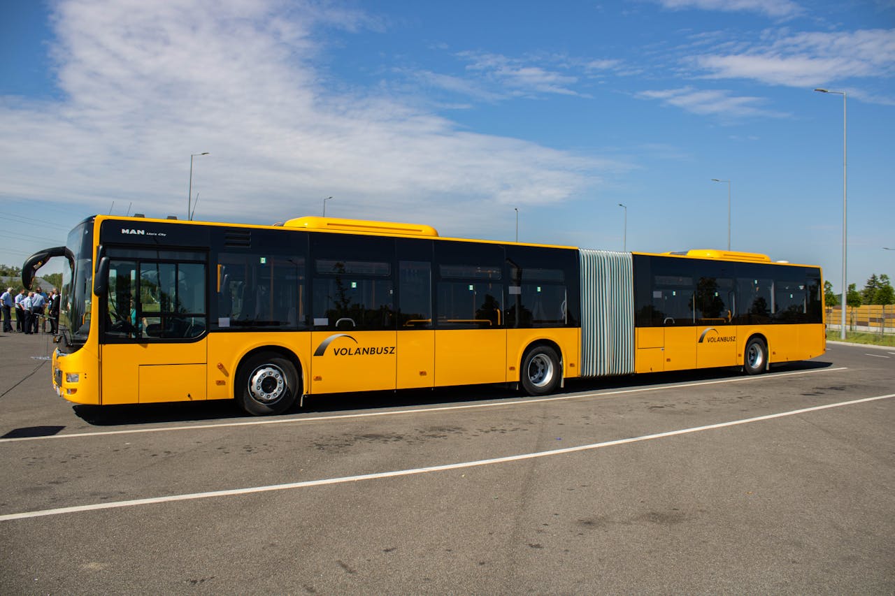 gallery-3 Yellow articulated city bus parked outdoors on a clear day in a spacious parking lot.