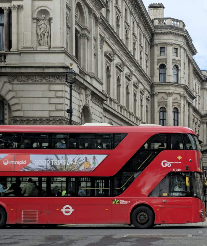 gallery-6 Classic red double-decker bus passing historic architecture on a London street, symbolizing urban travel.